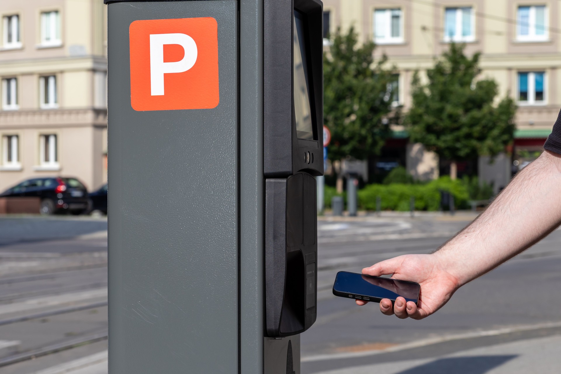 A person's hand uses a smartphone for contactless payment at a parking meter with a clear P symbol, symbolizing modern urban convenience and smart city technology